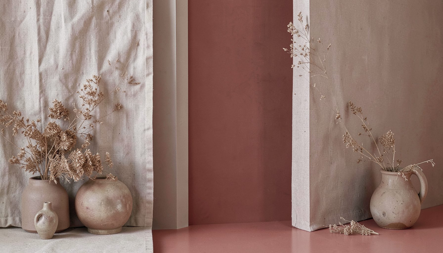 A serene composition of organic textures — linen, dried foliage, and ceramic vessels in muted earth tones
