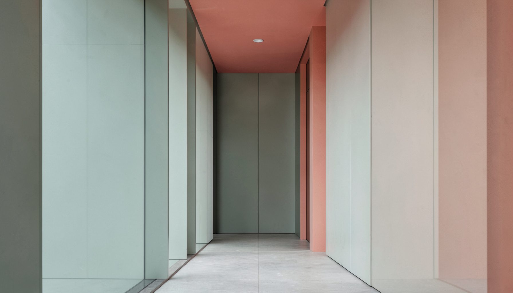 A clean architectural photograph with strong symmetry, soft natural light, and muted sage green and dusty coral accents